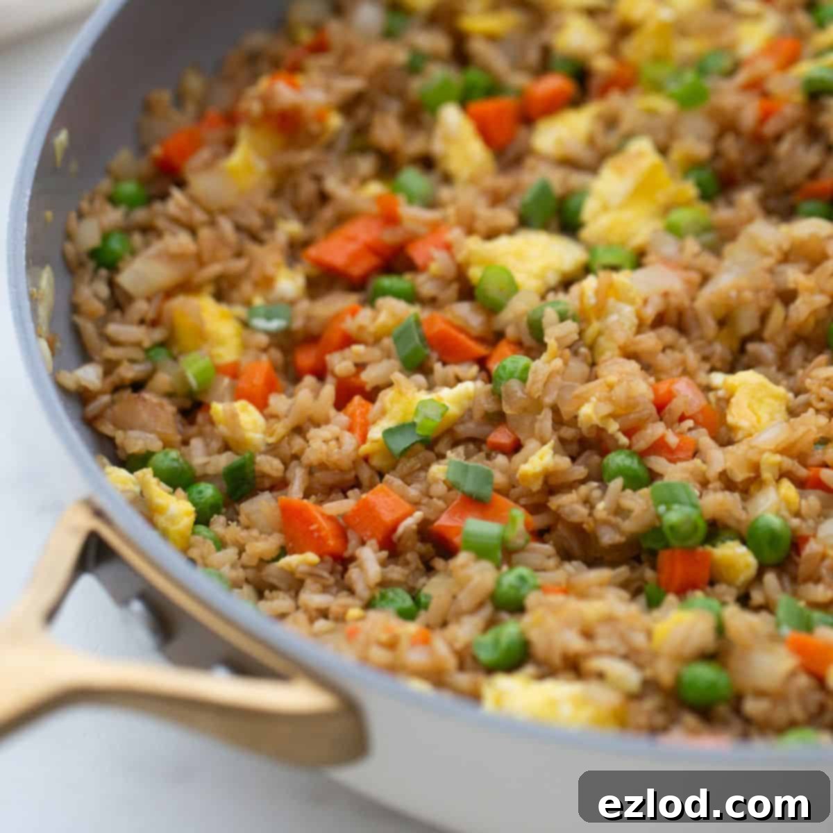 Wholesome Gluten-Free Hibachi Fried Rice 2 A large skillet filled with healthier hibachi fried rice, showcasing brown rice, vibrant peas, scrambled eggs, and diced carrots.