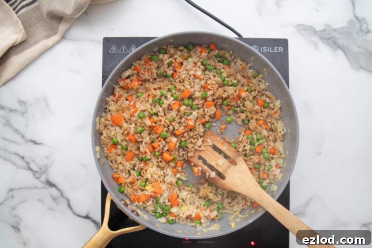 Wholesome Gluten-Free Hibachi Fried Rice 7 Cooked brown rice in a skillet being mixed with coconut aminos and scrambled eggs, ensuring all flavors are well combined.