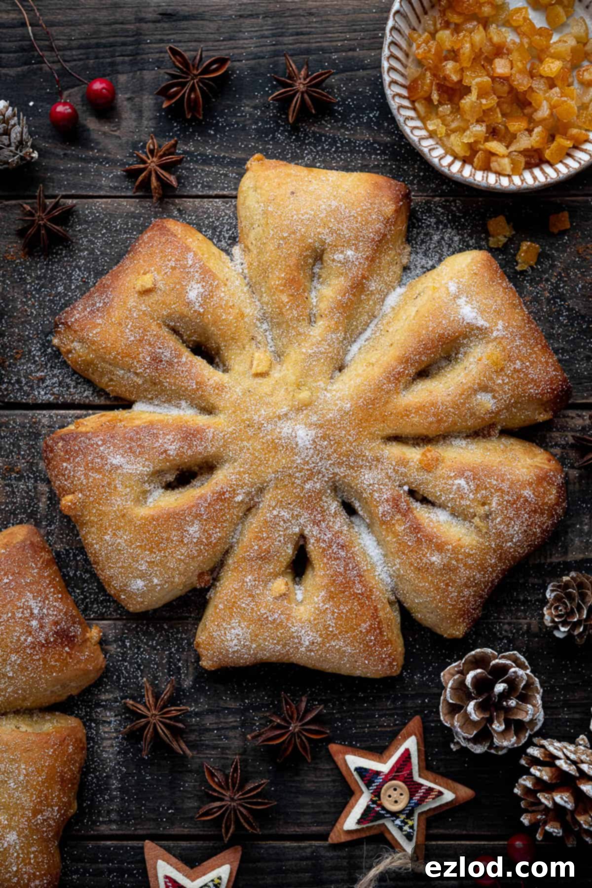 Orange and anise snowflake bread on a wooden background surrounded by Christmas decorations and a bowl of candied peel.