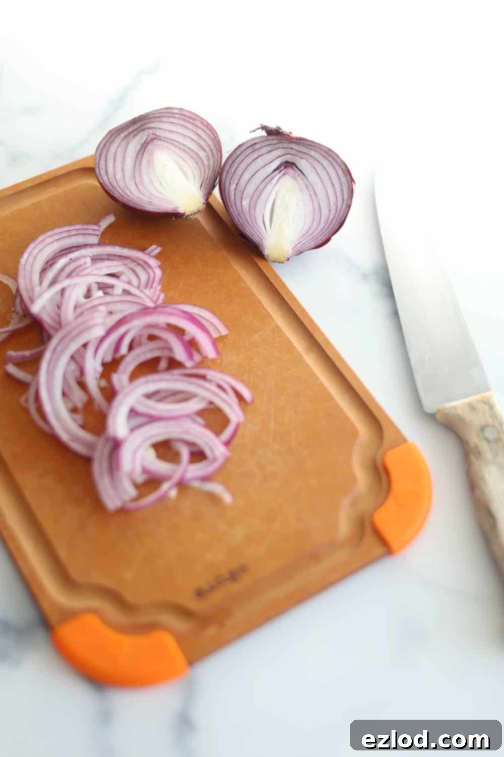 Thinly sliced red onions on a cutting board, ready for pickling for the Panera Green Goddess Cobb Salad.