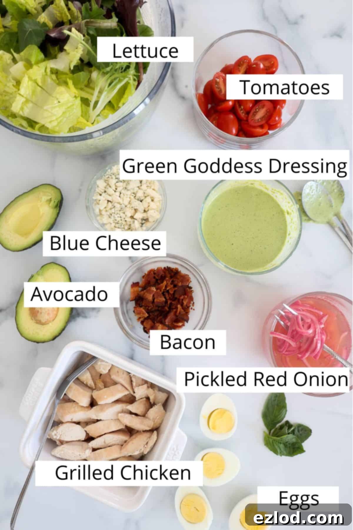 A collection of fresh ingredients laid out for the copycat Panera Green Goddess Cobb Salad, including greens, tomatoes, eggs, chicken, and avocado.
