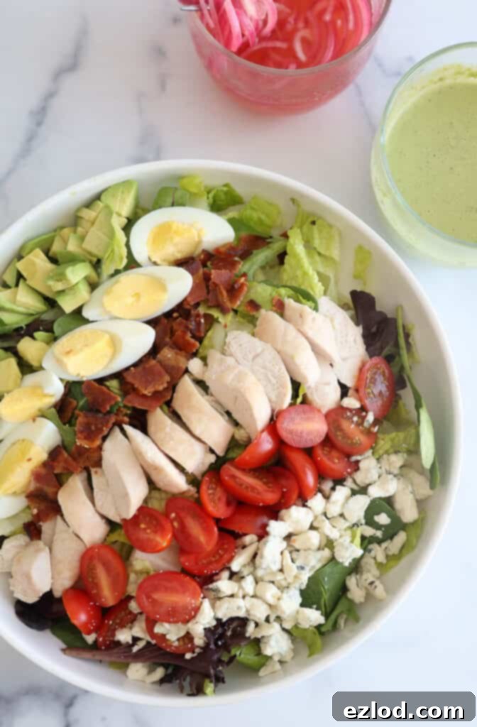 A bowl filled with the base ingredients for Copycat Panera Cobb Salad, including greens, tomatoes, bacon, eggs, chicken, and cheese.