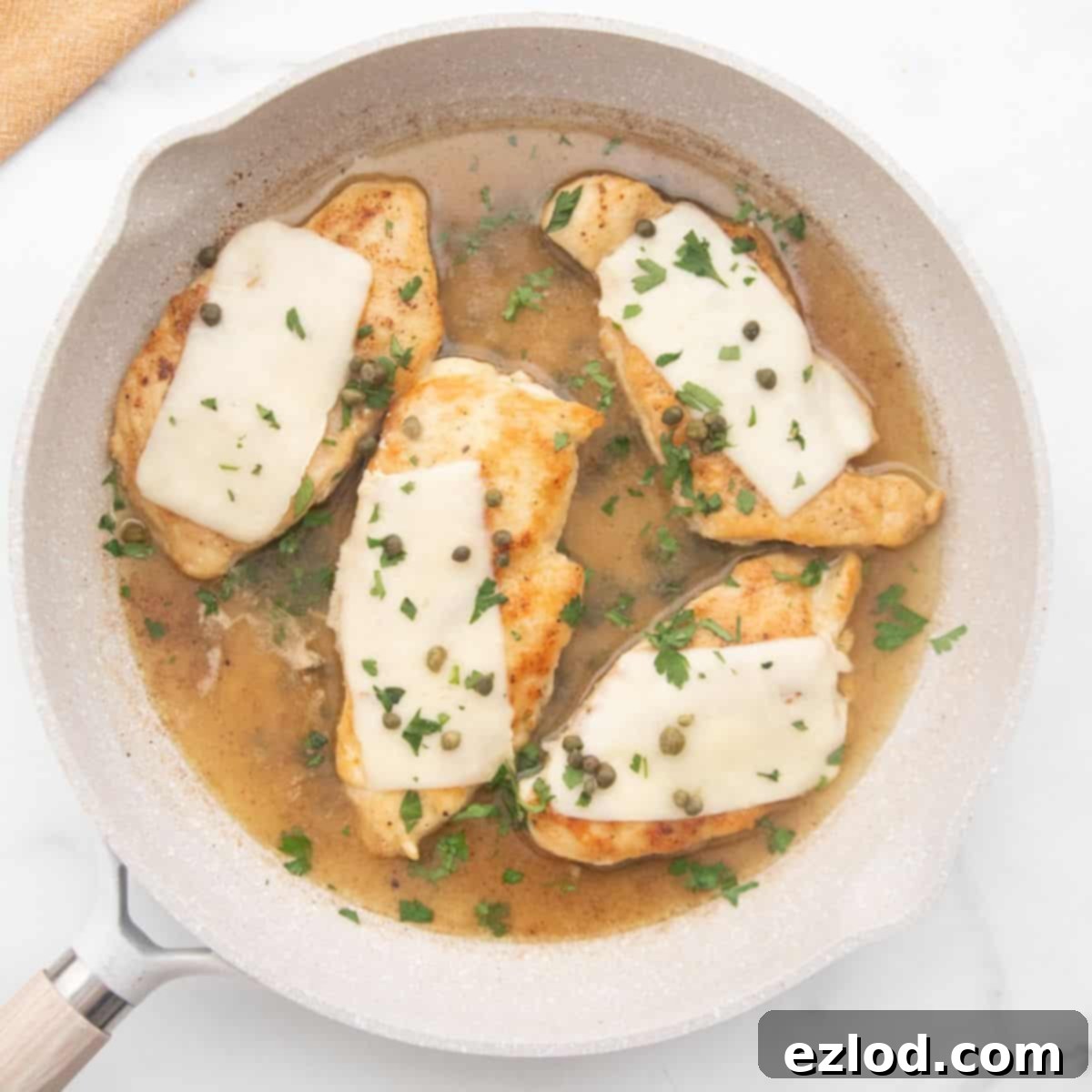 Weeknight Chicken Scallopini 2 Chicken scallopini in a white ceramic pan topped with thin mozzarella, capers, and fresh parsley.