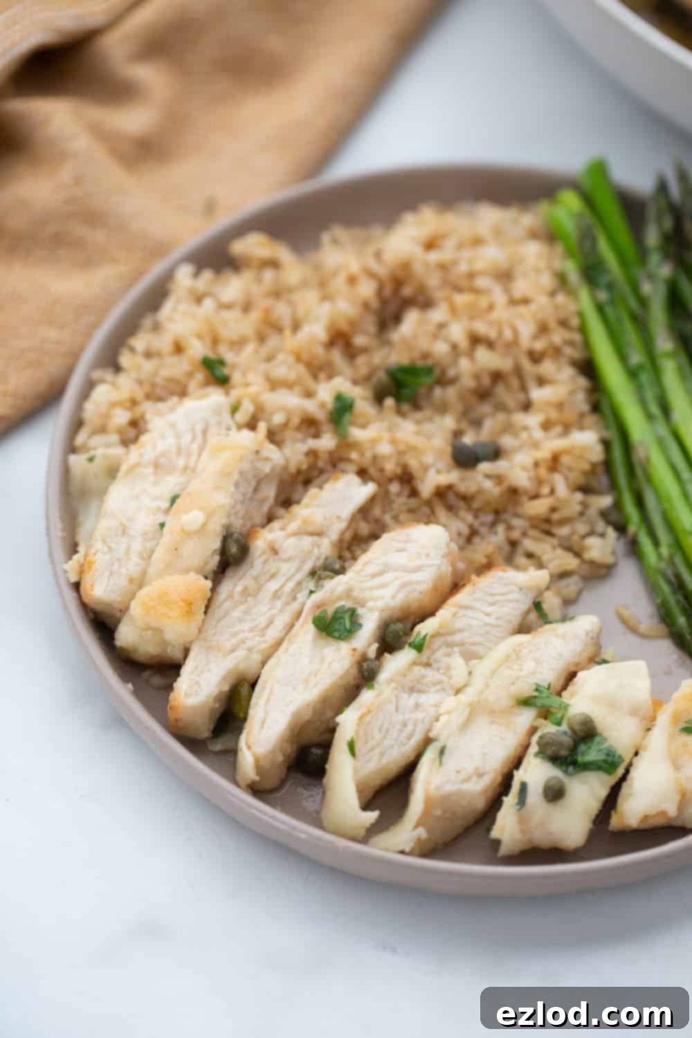 Weeknight Chicken Scallopini 4 Chicken Scallopini served with roasted asparagus and brown rice shown sliced on a neutral colored rimmed plate.