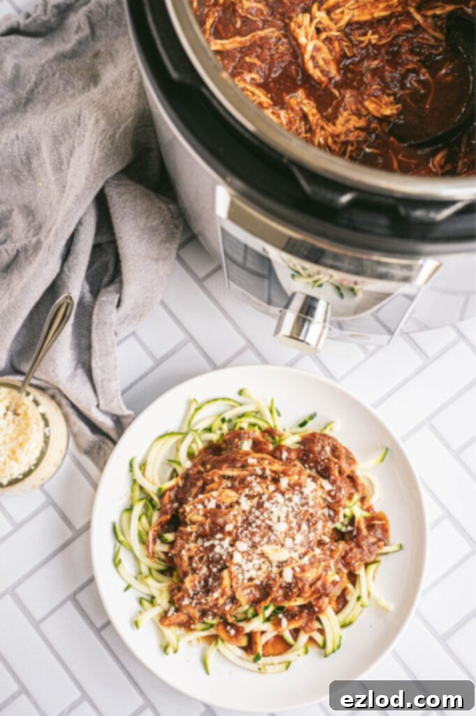 Overhead photo of chicken in the Instant Pot with a plate of chicken and zoodles on a white, tile counter top.