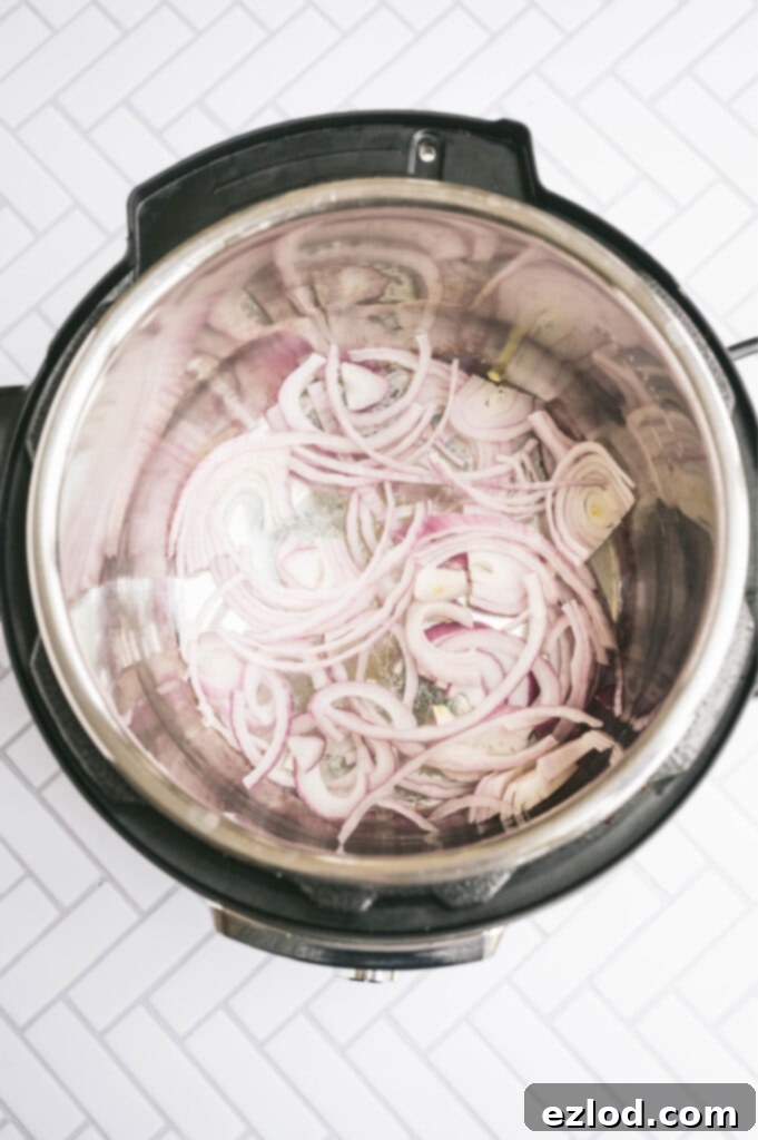Overhead photo of red onion sauteing in the instant pot on a white tile surface.