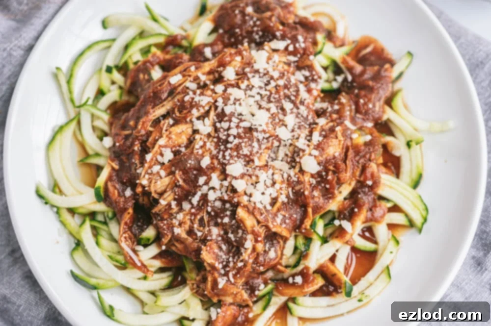 Close up photo of zoodles topped with Instant Pot Balsamic chicken, sprinkled with parmesan cheese. These are on a white plate with a gray linen background.