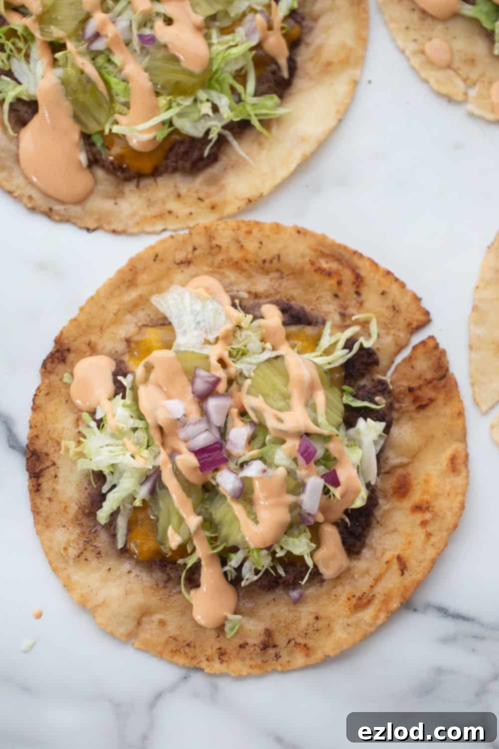Two vibrant gluten-free Big Mac tacos on a white plate, showcasing their rich toppings of shredded lettuce, creamy Big Mac sauce, bright green pickle slices, and aromatic diced red onions, ready to be enjoyed.