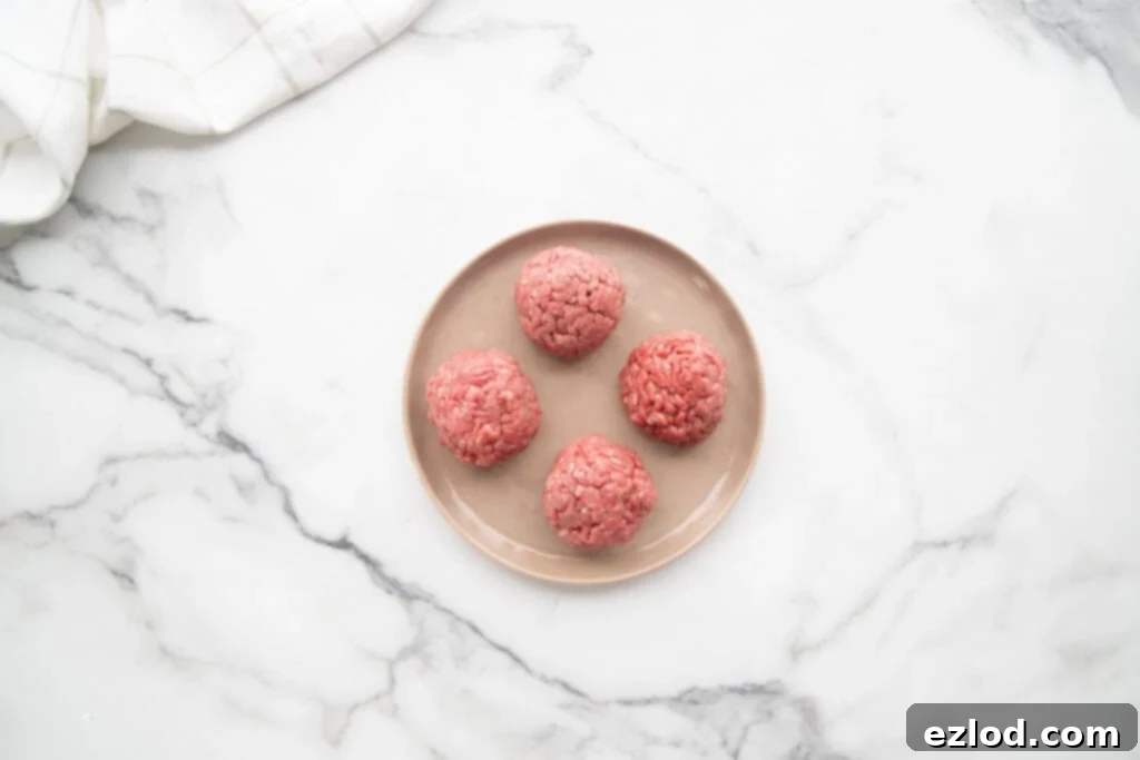 A neat arrangement of one pound of lean ground beef, precisely divided into four equal, hand-rolled balls, set on a small white plate, ready for the smash burger taco preparation.