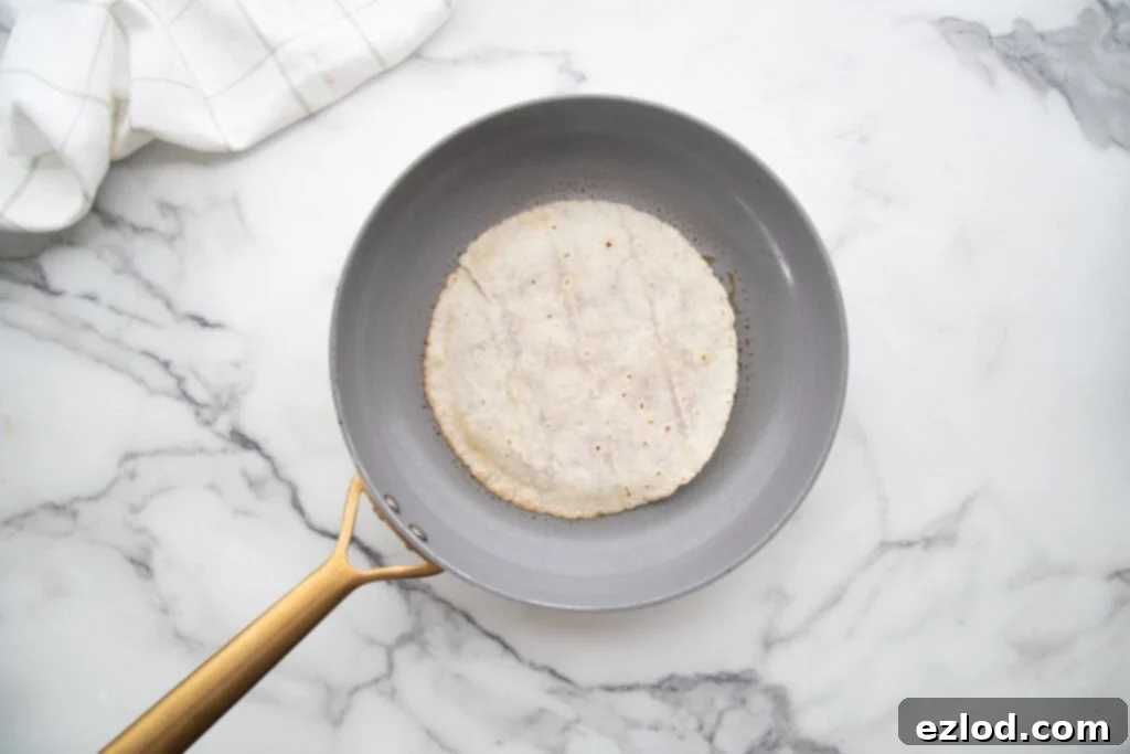 A single white gluten-free tortilla, with its thinly pressed raw beef patty side down, expertly searing in a preheated ceramic non-stick pan, beginning to develop a rich brown crust.