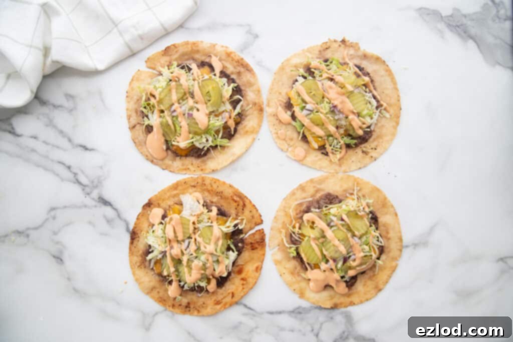 Two fully assembled gluten-free Big Mac tacos, artfully garnished with a generous pile of fresh shredded lettuce, a luscious drizzle of the homemade special sauce, tangy dill pickle slices, and finely diced onions, beautifully presented and ready to eat.