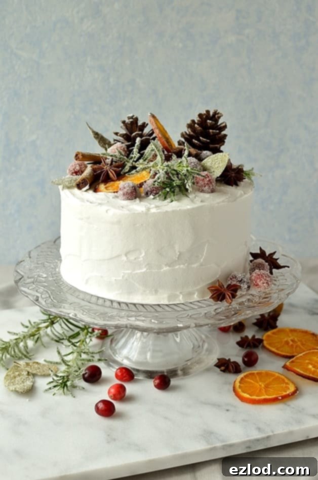 Moist, gingery Christmas fruitcake topped with marzipan, royal icing and rustic decorations of sugared cranberries, rosemary and bay leaves, dried orange slices, pine cones and whole spices.