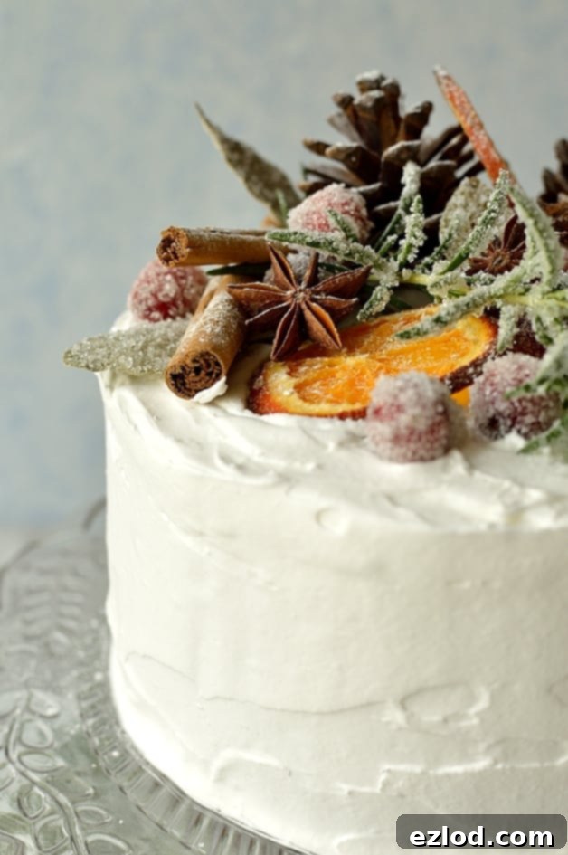 Moist, gingery fruitcake topped with marzipan, royal icing, sugared cranberries, rosemary and bay leaves, dried orange slices, pine cones and whole spices.