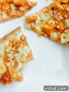 Buffalo chicken flatbread pizza cut into triangles on a white background. One of the triangles has bites taken out of it, showcasing the layers of cheese and chicken, inviting a taste.