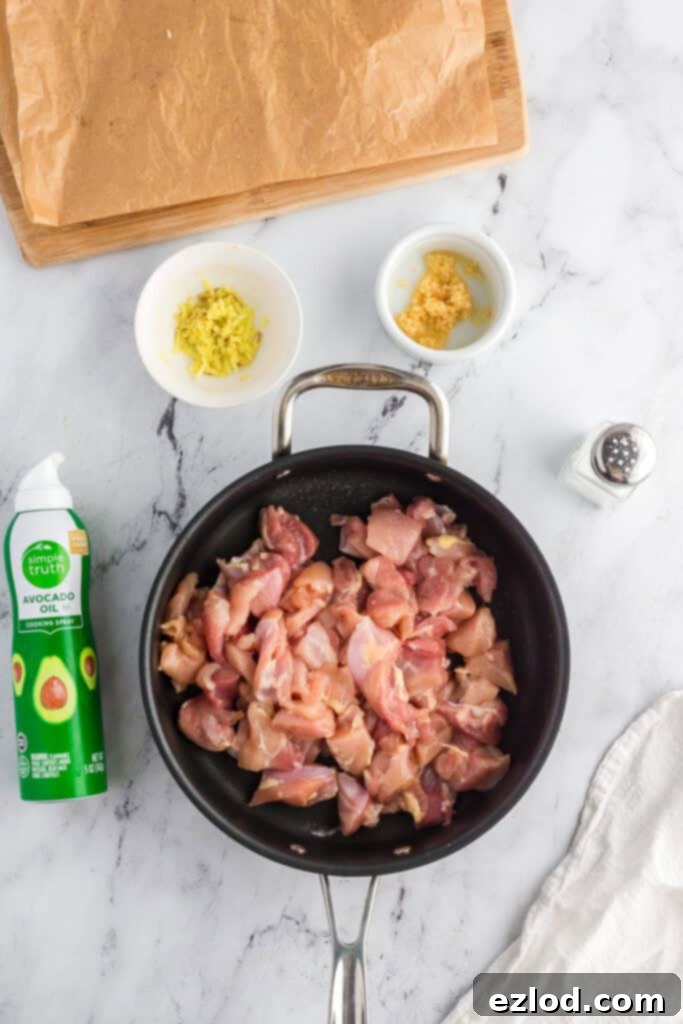 Raw chicken thighs seasoned with salt and cooking in a pan with avocado oil spray, minced fresh ginger, and garlic.