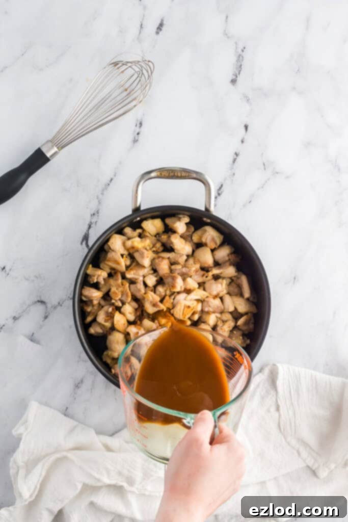 Thick, glossy bourbon sauce being poured over perfectly cooked chicken in a pan.
