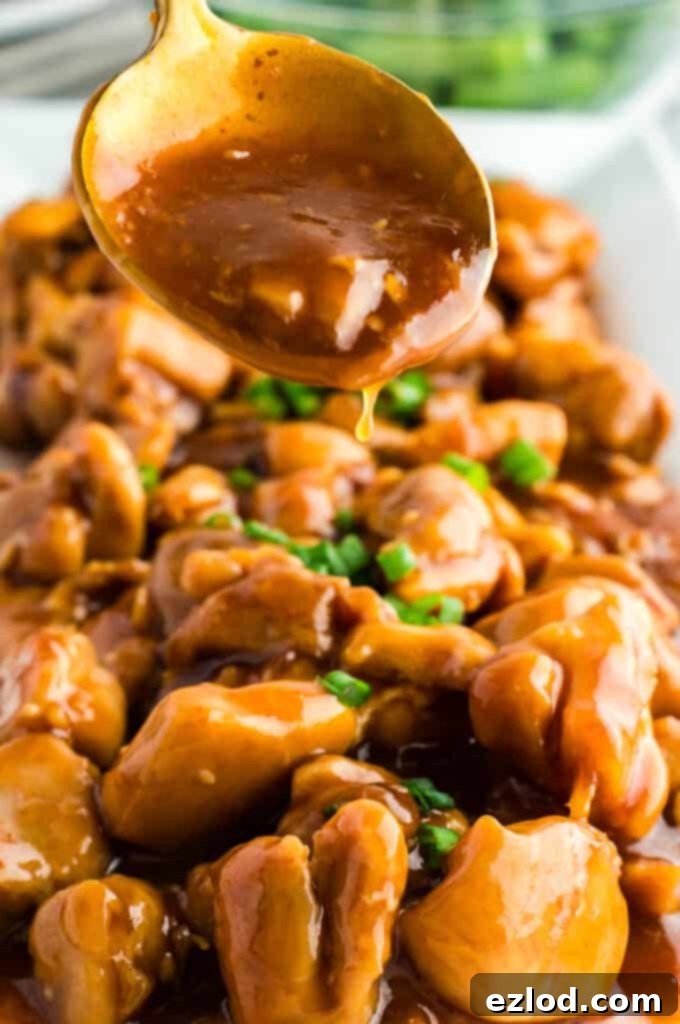 Finished bourbon chicken, glistening with sticky sauce, garnished with fresh green onions in a pan.