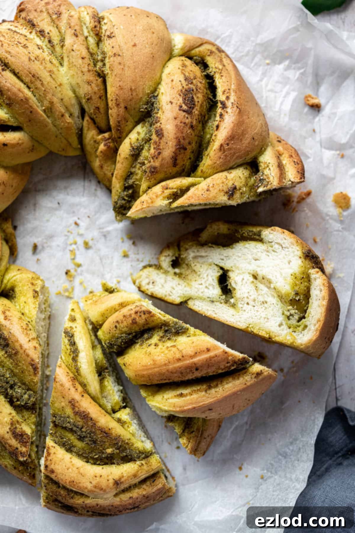 A close-up view of golden-brown slices of vegan pesto bread, revealing the beautiful green pesto swirls within the soft, fluffy bread. The slices are stacked, highlighting the intricate layers and inviting texture of the bread.