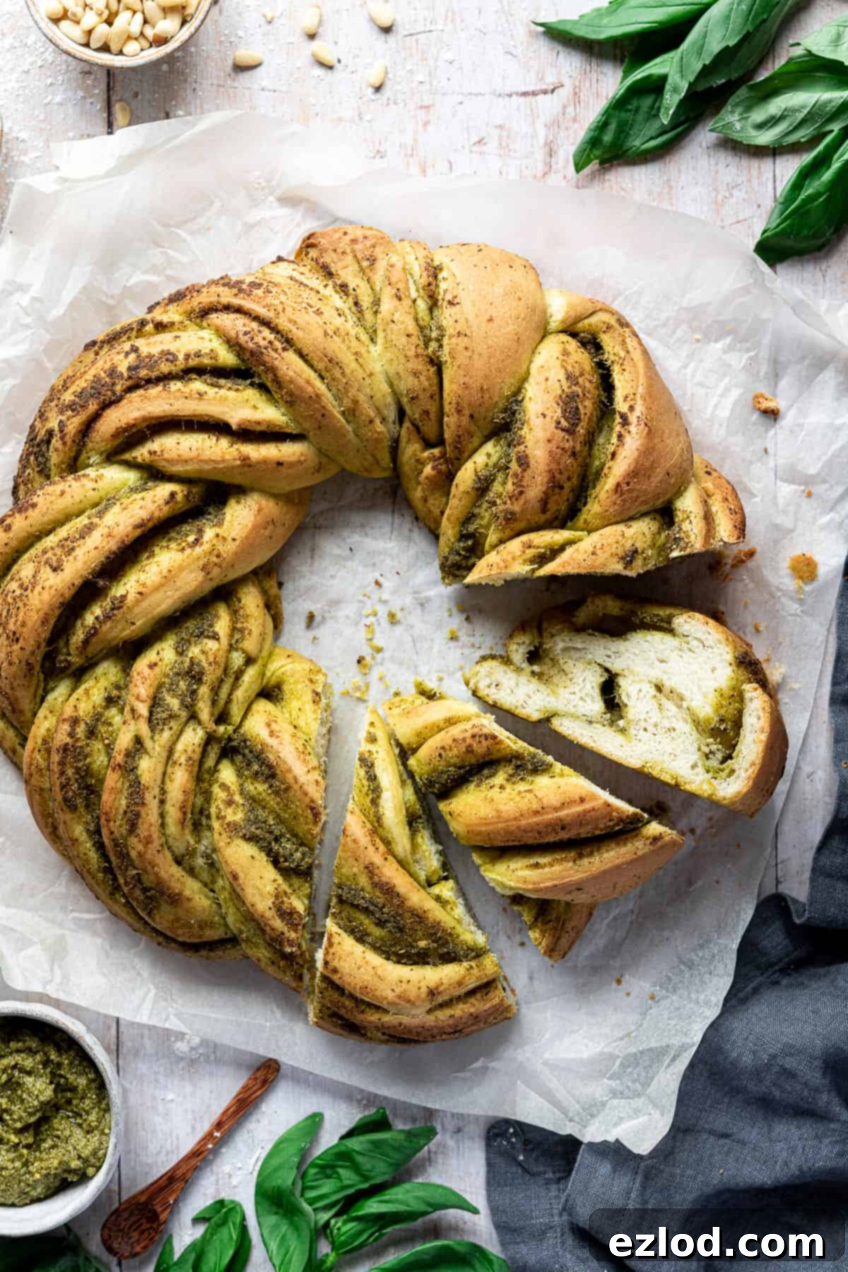 A beautiful close-up of a portion of vegan pesto bread, showing the intricate swirls of green pesto within the golden-brown crust and soft, airy crumb. It rests on a sheet of white baking parchment, highlighting its delicious texture and vibrant color.