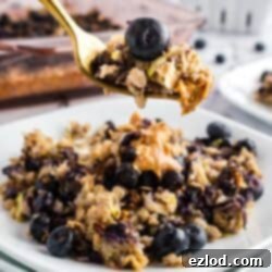 A serving of zucchini blueberry baked oatmeal on a white plate, garnished with fresh blueberries and a gold fork.