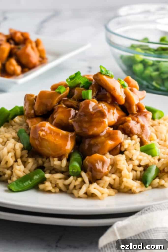 Easy homemade bourbon chicken plated over brown rice with green beans and garnished with green onions.