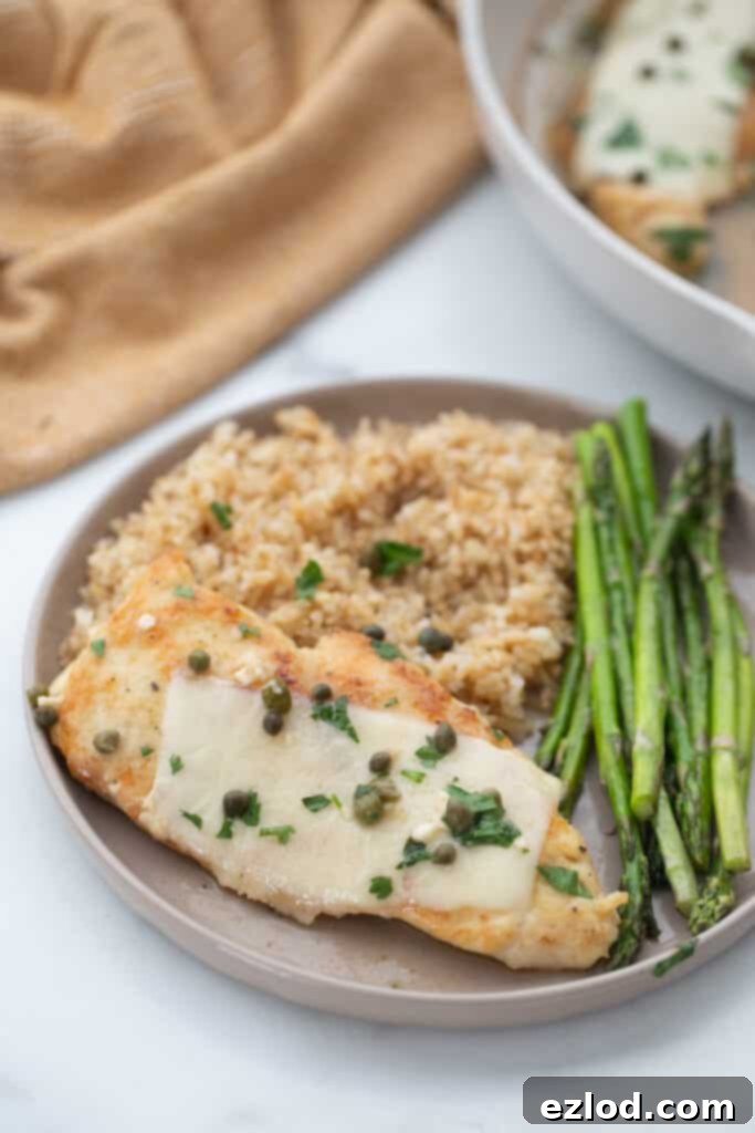 Plated dinner with thinly sliced chicken in a lemon butter sauce with brown rice and roasted asparagus.