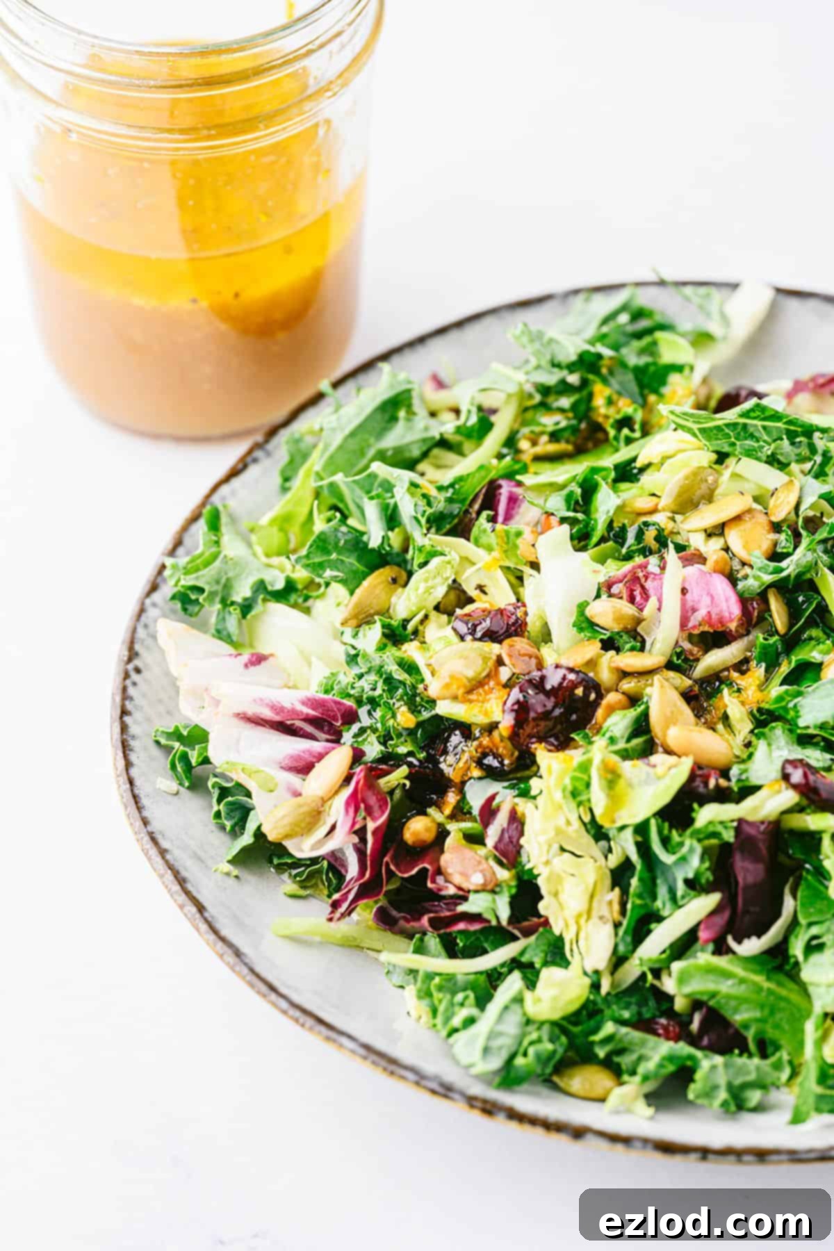 A jar of freshly mixed apple cider vinaigrette next to a holiday salad, showcasing its vibrant color.