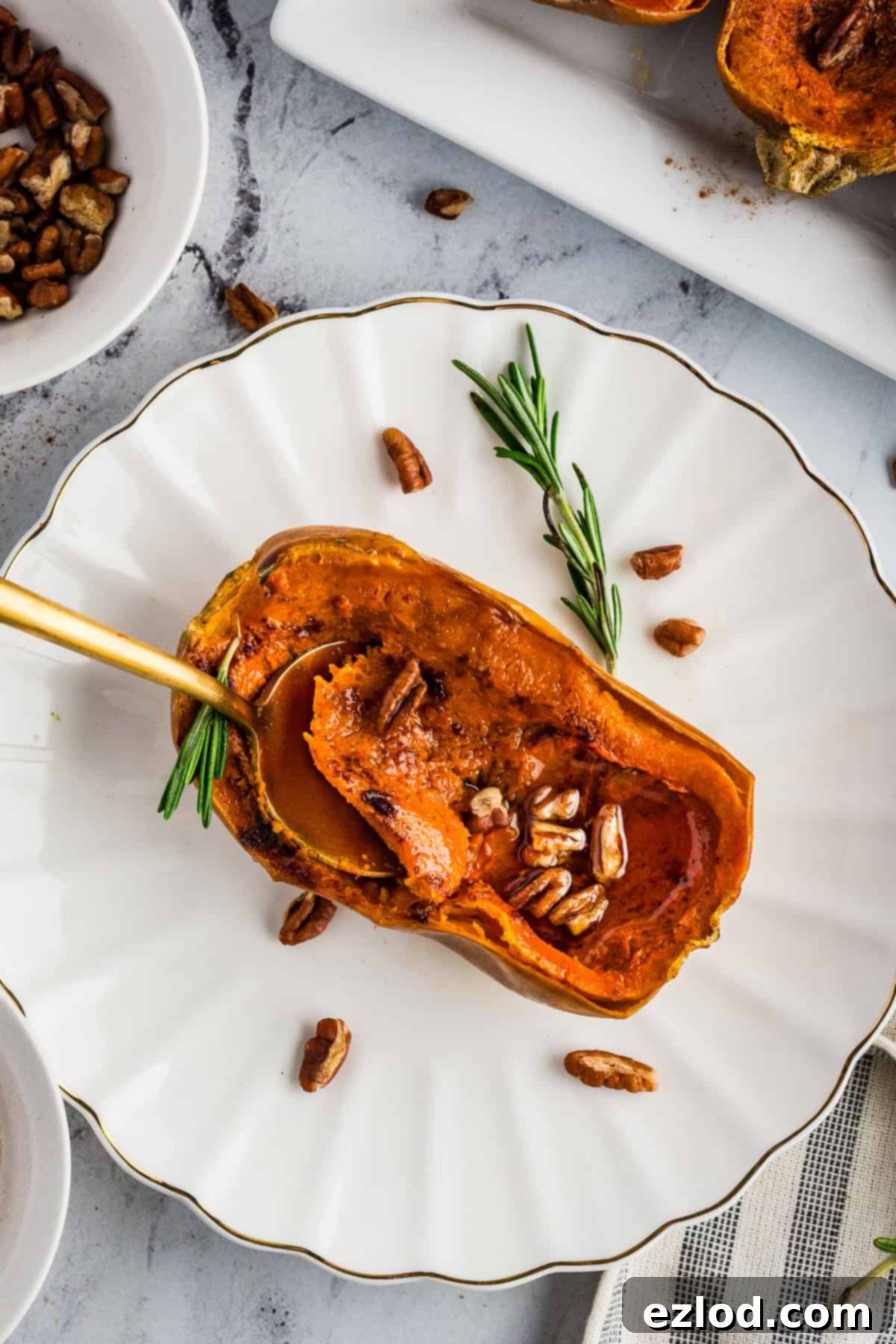 Sweet Maple Roasted Honeynut Squash Air Fryer Oven 3 A beautifully roasted honeynut squash half resting on a pristine white plate, generously drizzled with golden maple syrup and topped with crunchy pecans and a fragrant sprig of rosemary.
