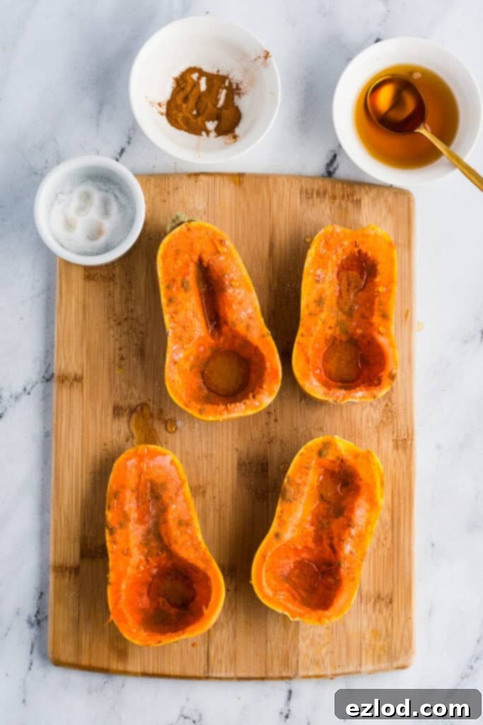 Sweet Maple Roasted Honeynut Squash Air Fryer Oven 6 Honeynut squash halves on a cutting board, expertly brushed with glossy maple syrup and evenly seasoned with a dusting of salt and cinnamon, with the seasoning ingredients artfully arranged nearby.