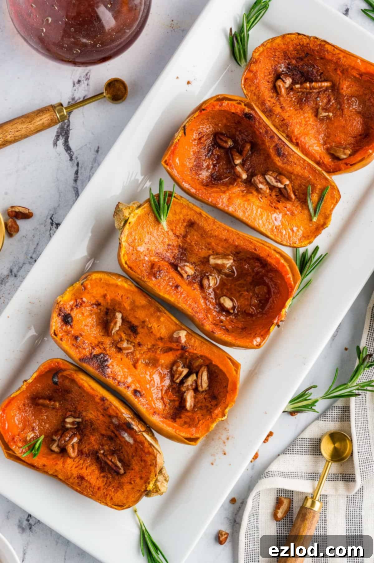 Sweet Maple Roasted Honeynut Squash Air Fryer Oven 10 A elegant white platter showcasing roasted honeynut squash, artfully garnished with vibrant fresh rosemary sprigs and a scattering of finely chopped pecans, making for a beautiful presentation.