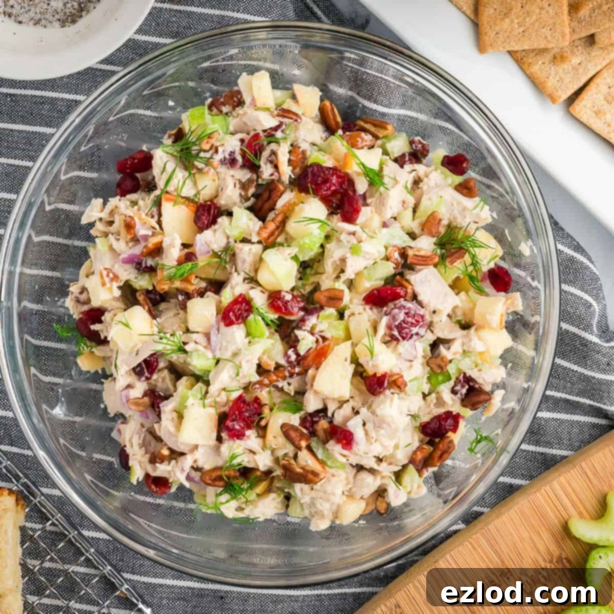 The fully mixed leftover turkey salad in a clear bowl, showing generous chunks of turkey, diced apple, dried cranberries, and chopped pecans coated in a creamy, light dressing, all set on a pristine white marble tabletop.