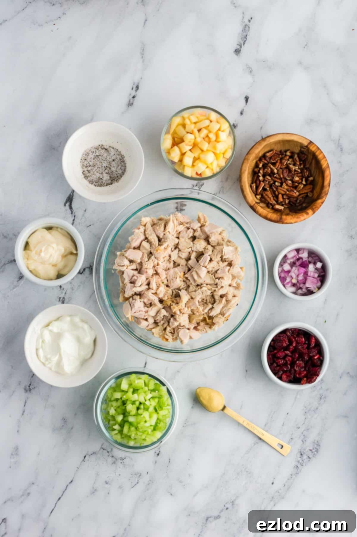 A vibrant flat lay image showcasing all the fresh and prepared ingredients for the leftover turkey salad, including diced turkey, chopped apple, celery, red onion, pecans, dried cranberries, mayonnaise, Greek yogurt, and Dijon mustard, arranged on a rustic wooden board.