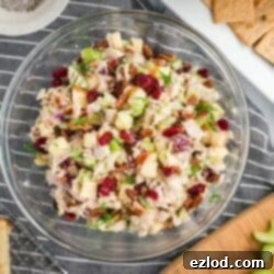 The fully mixed turkey salad in a clear bowl, showing chunks of turkey, diced apple, cranberries, and pecans coated in a creamy dressing on a white marble tabletop.