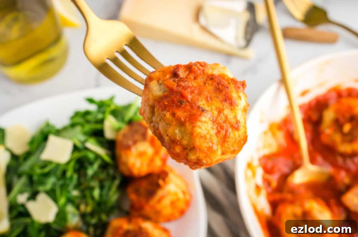 A fork holding a chicken meatball covered in sauce.