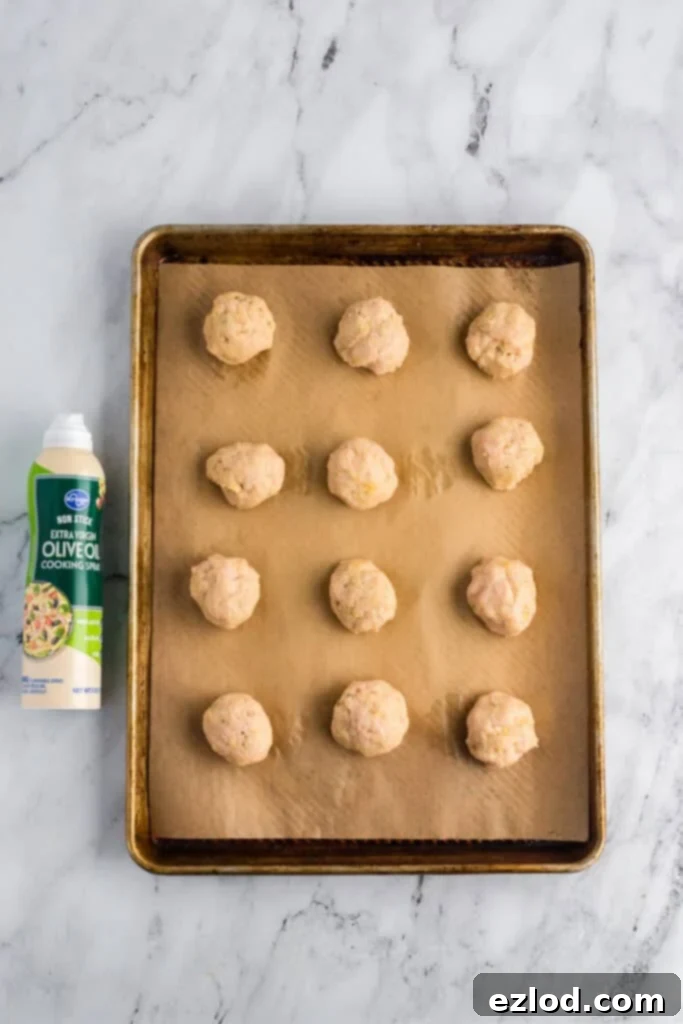 Parchment lined sheet pan with raw chicken meatballs sitting next to olive oil cooking spray.