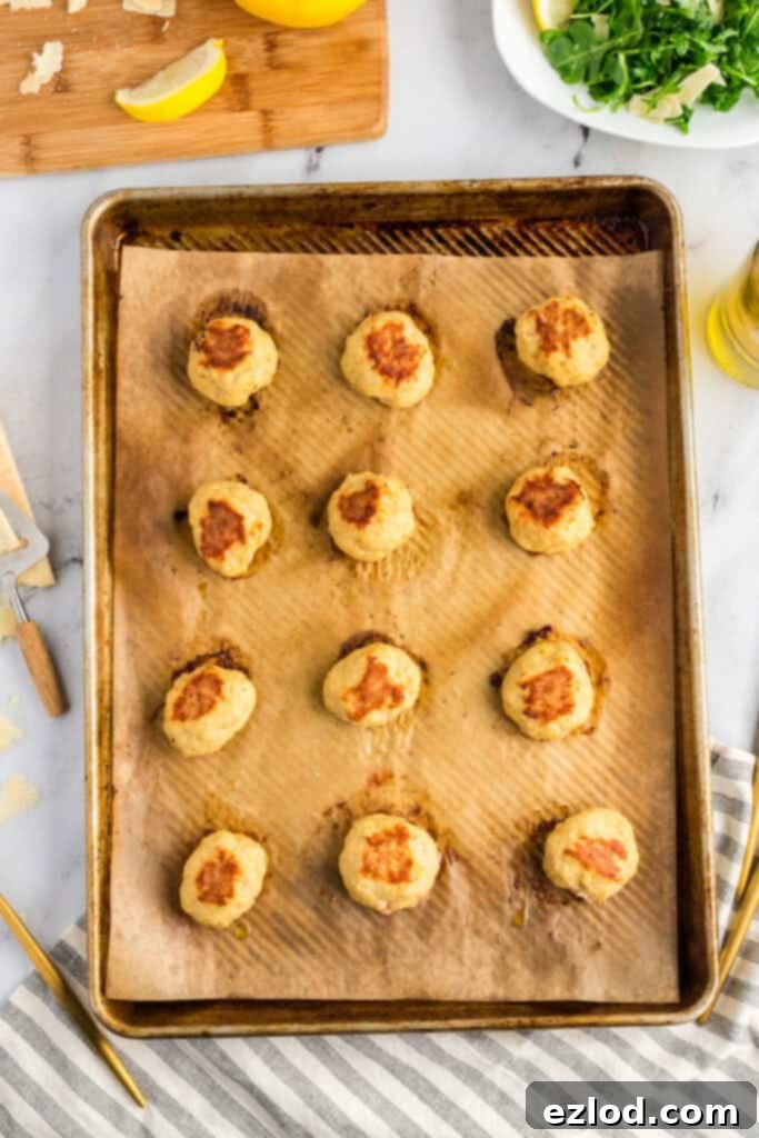 Browned baked chicken meatballs on a sheet pan covered with parchment paper.