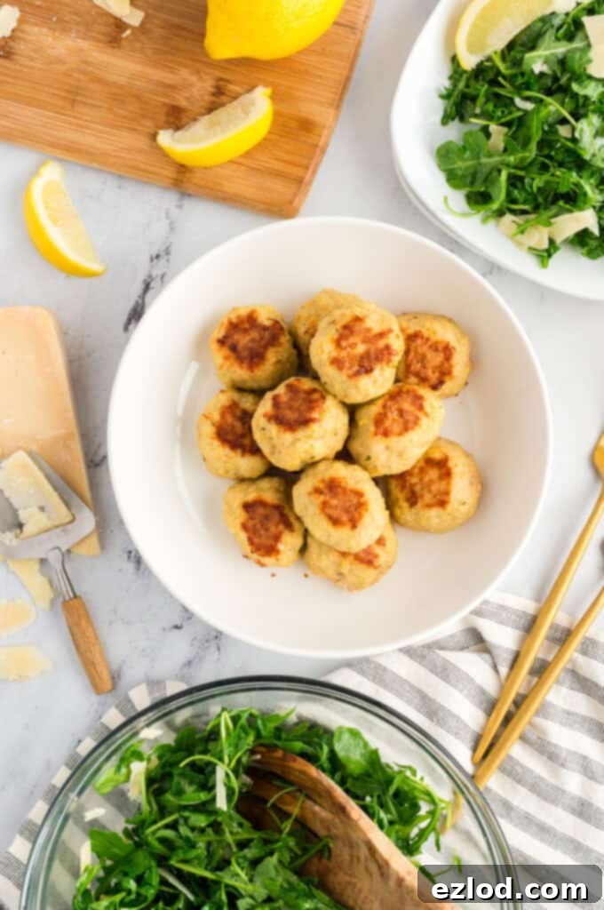 Overhead shot of chicken meatballs on a white table with a serving bowl and plate of arugula salad.