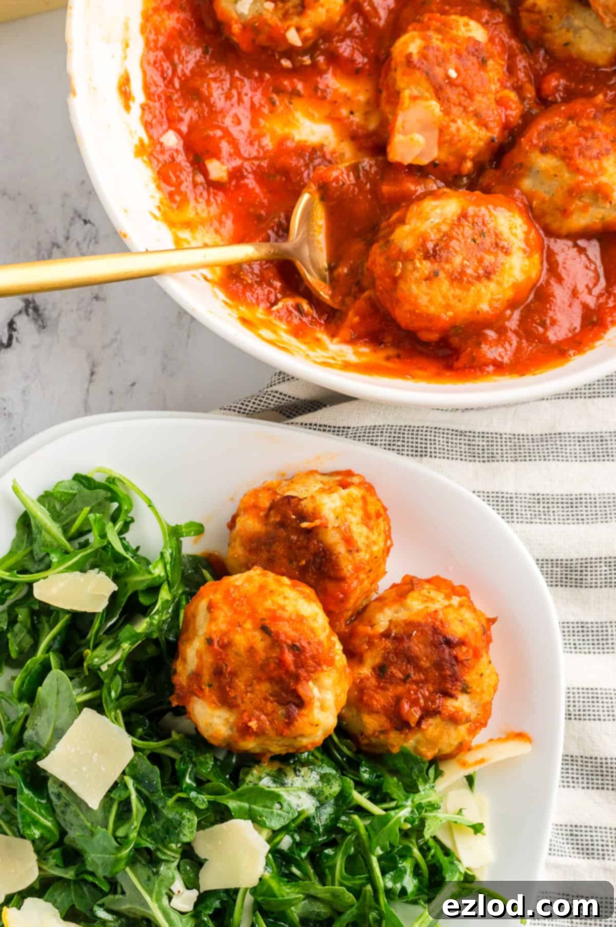 A serving bowl of chicken meatballs next to a plate of salad and meatballs.