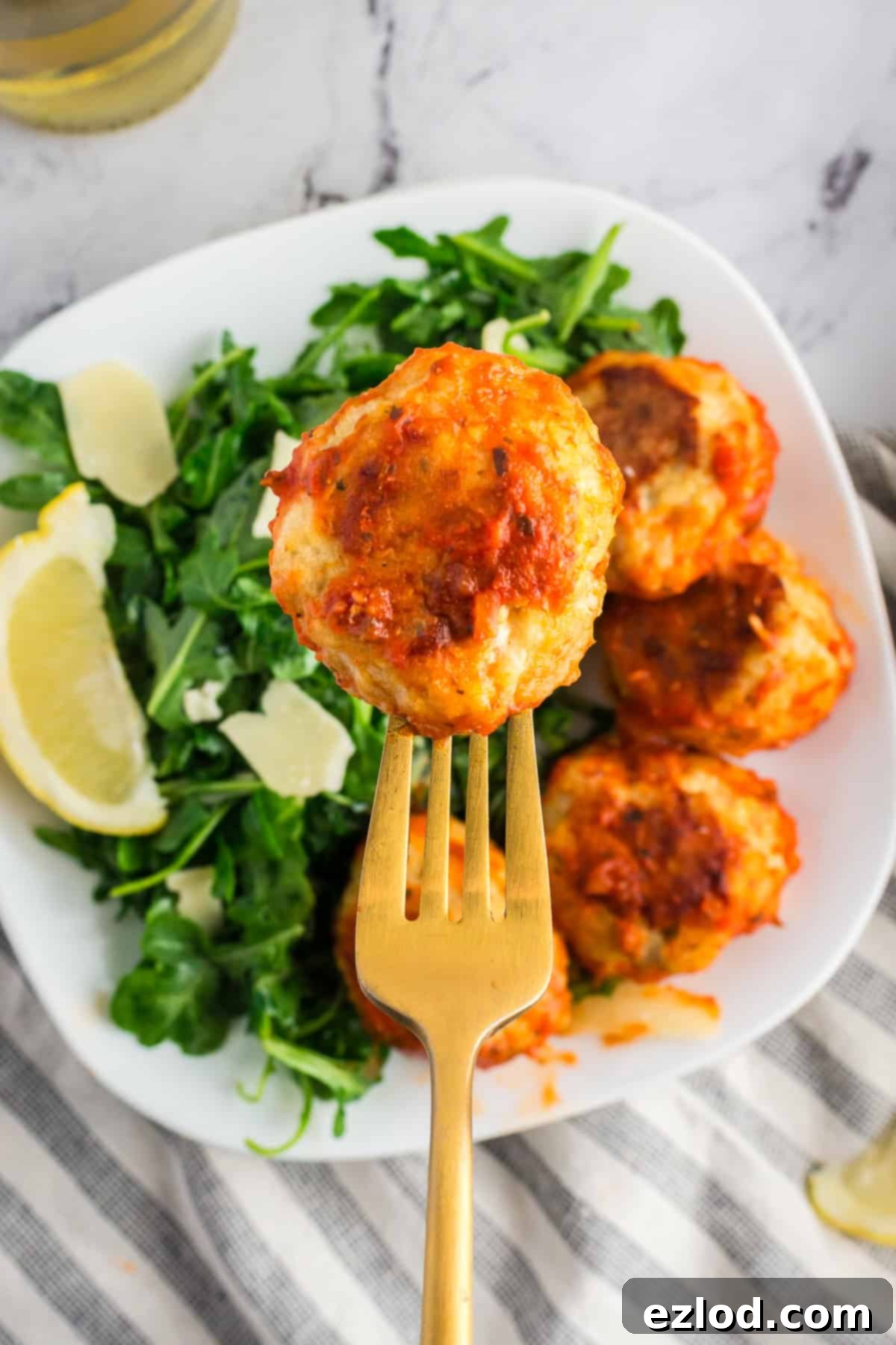 A fork holiday a baked chicken meatball covered in sauce over a bowl of arugula.