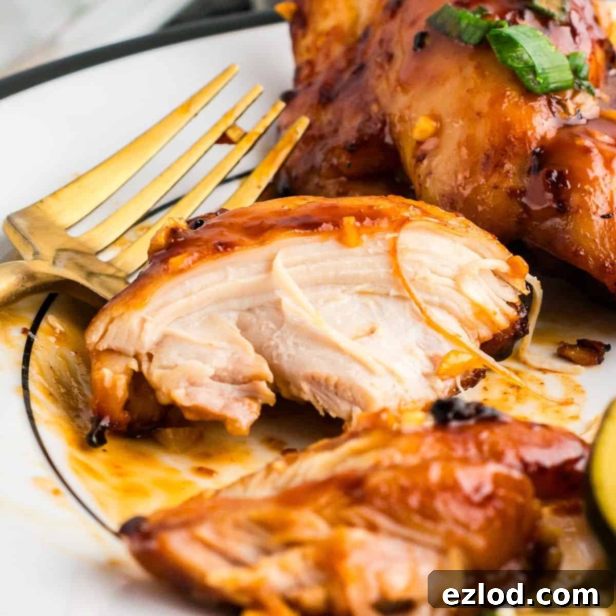 Glazed Sticky Chicken Thighs: Air Fried or Oven Baked 2 A piece of chicken thigh on a white plate with a gold fork, showcasing the sticky glaze.
