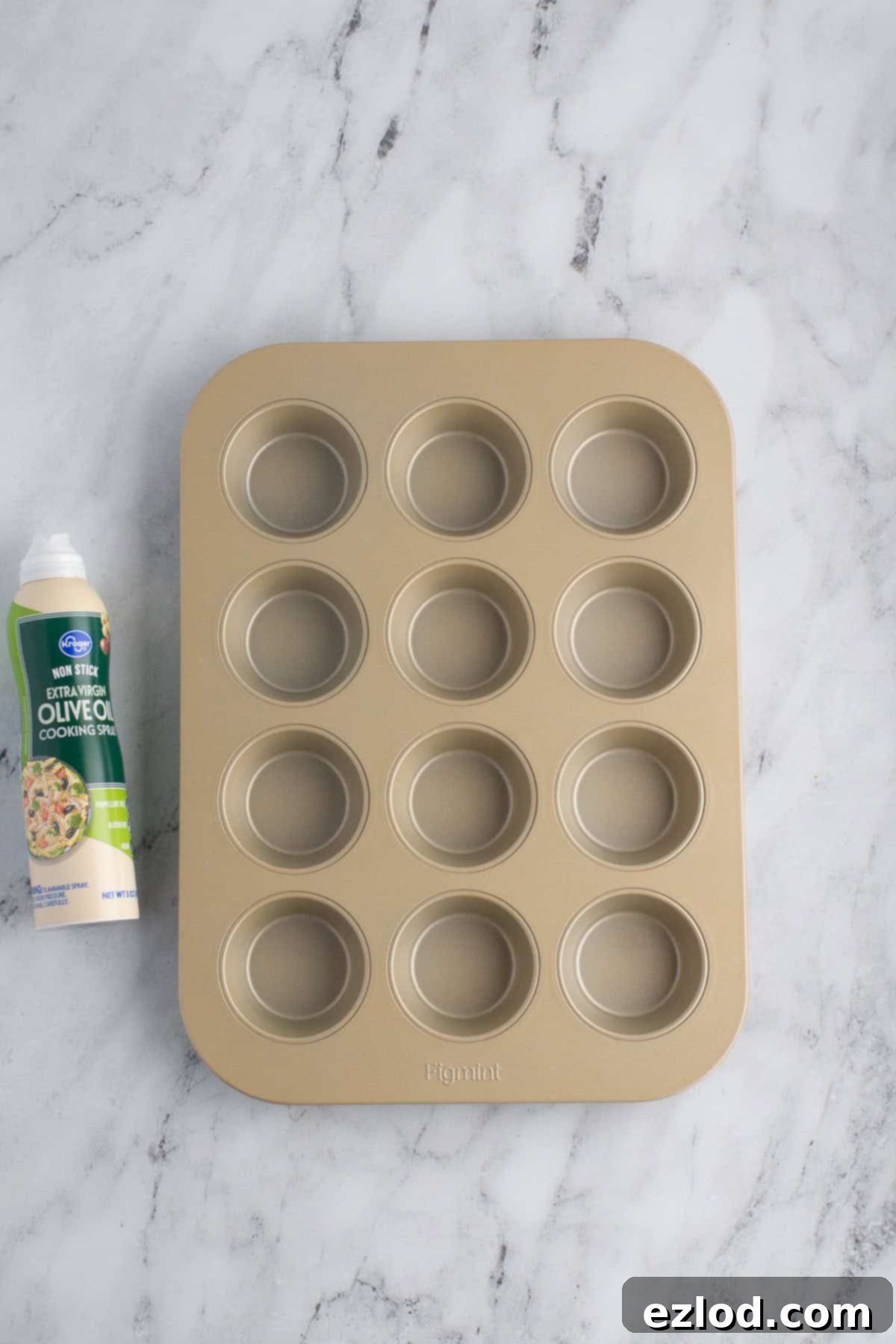 An empty muffin tin with baking spray laying next to it on a marble background.