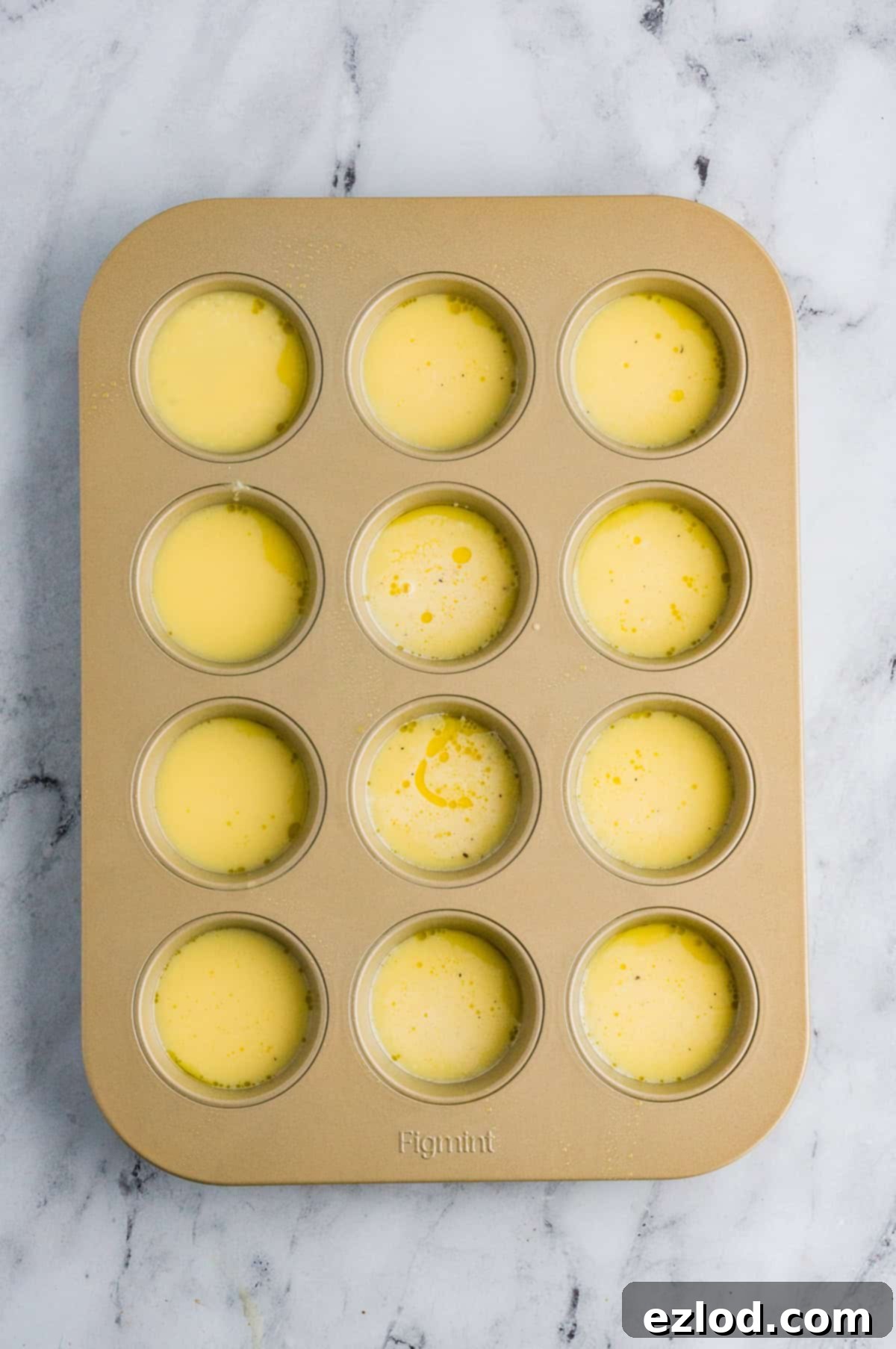 Egg mixture in a prepared muffin tin on a marble background.