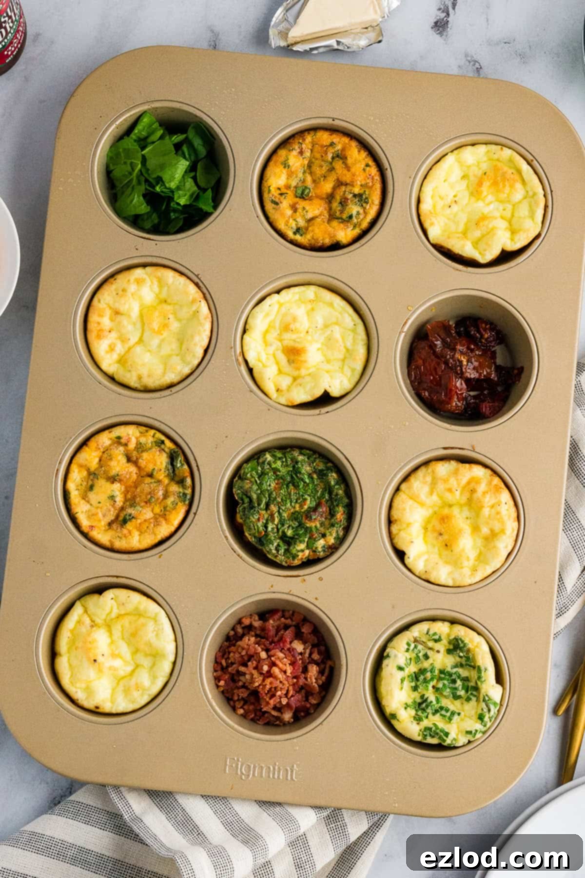 Egg bites pictured in a muffin tin with extra fixings in three of the tins.