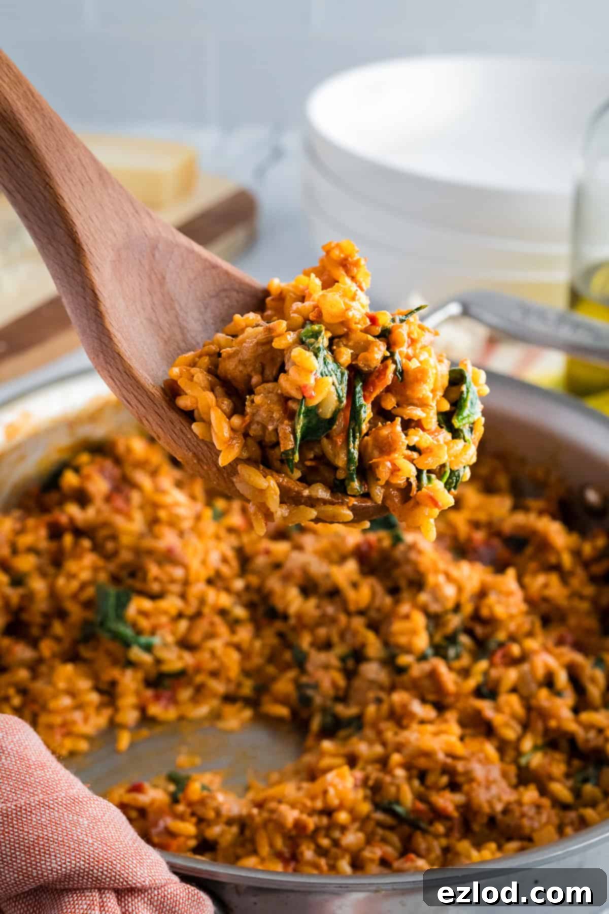 A large wooden spoon scooping a generous portion of Marry Me Chicken Orzo from a skillet, showing its creamy texture before being plated.