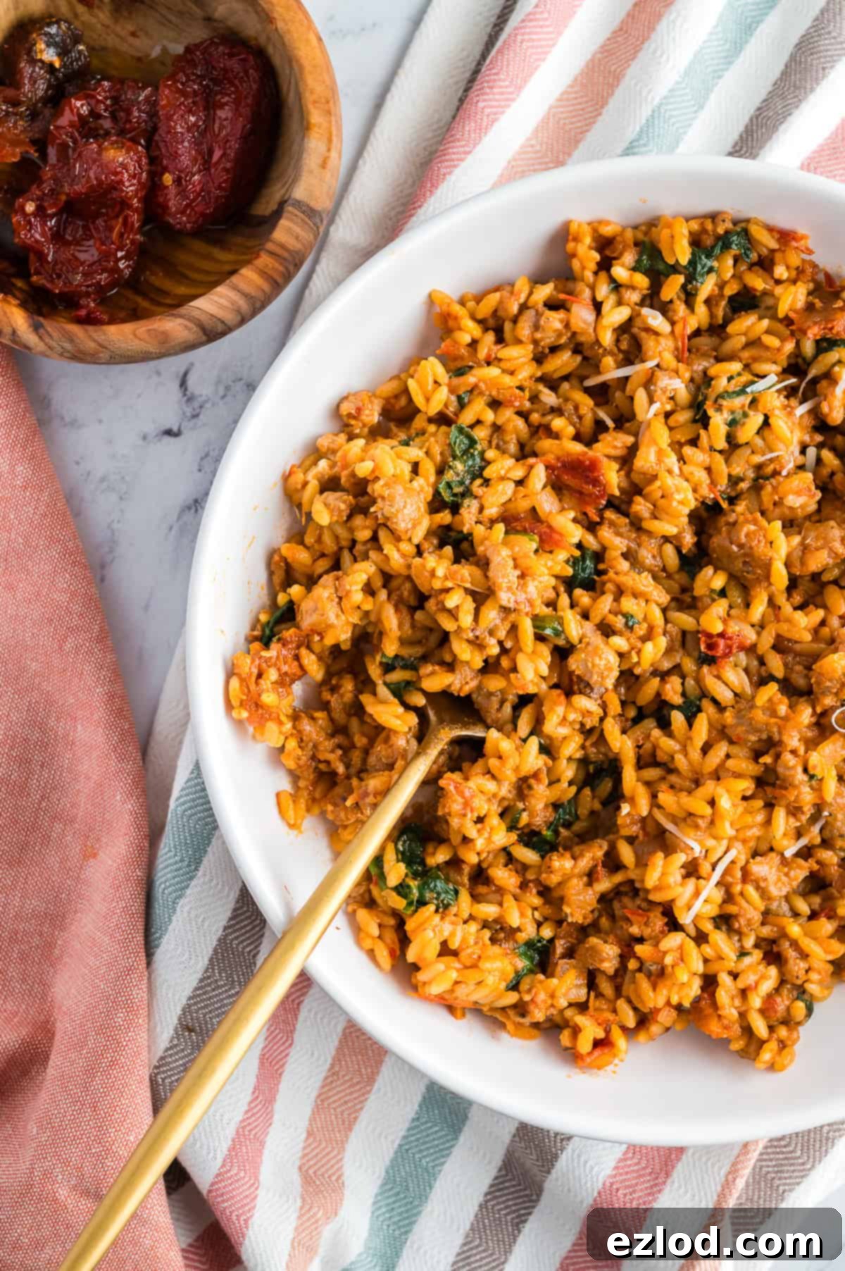 A white serving bowl filled with a large portion of Marry Me Chicken Orzo, featuring a gold-colored spoon resting inside the creamy pasta.
