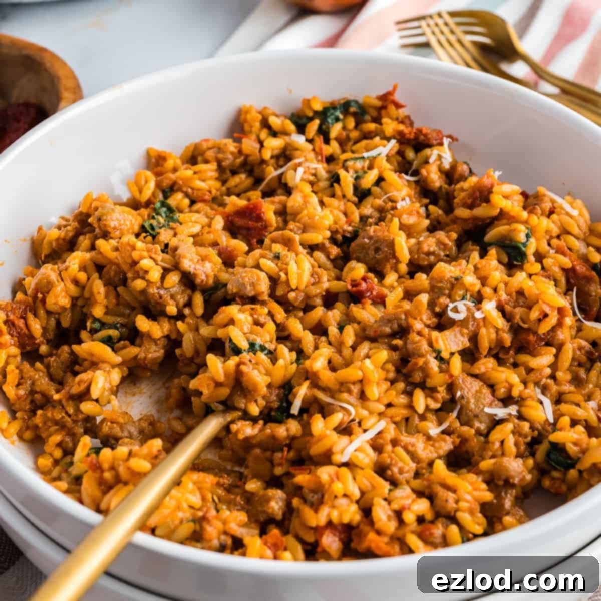 A white bowl filled with creamy Marry Me Chicken Orzo, with a gold spoon partially submerged in the dish.