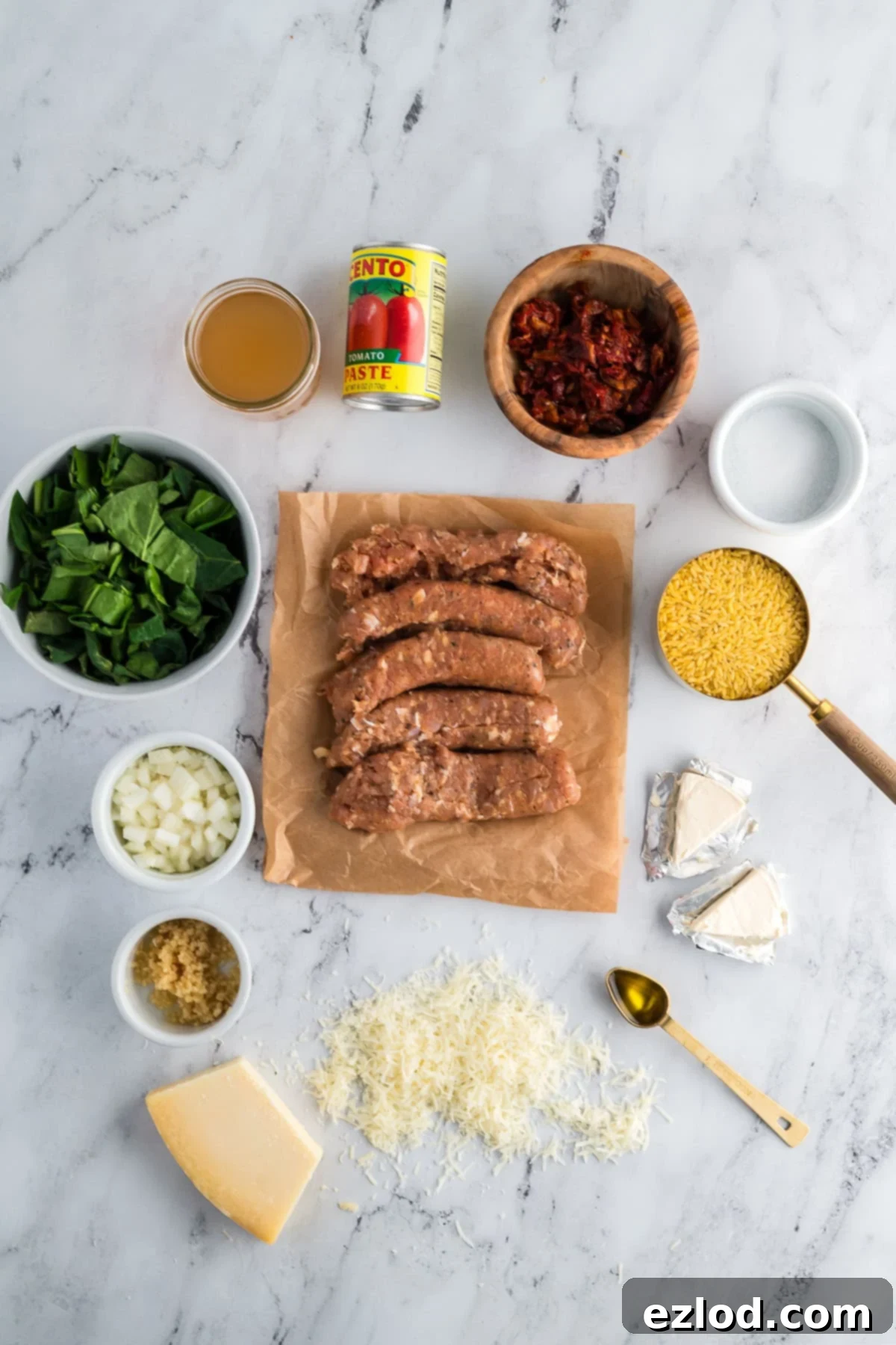 Various ingredients for Marry Me Chicken Orzo laid out on a marble surface, including chicken sausage, sun-dried tomatoes, orzo, and spinach.