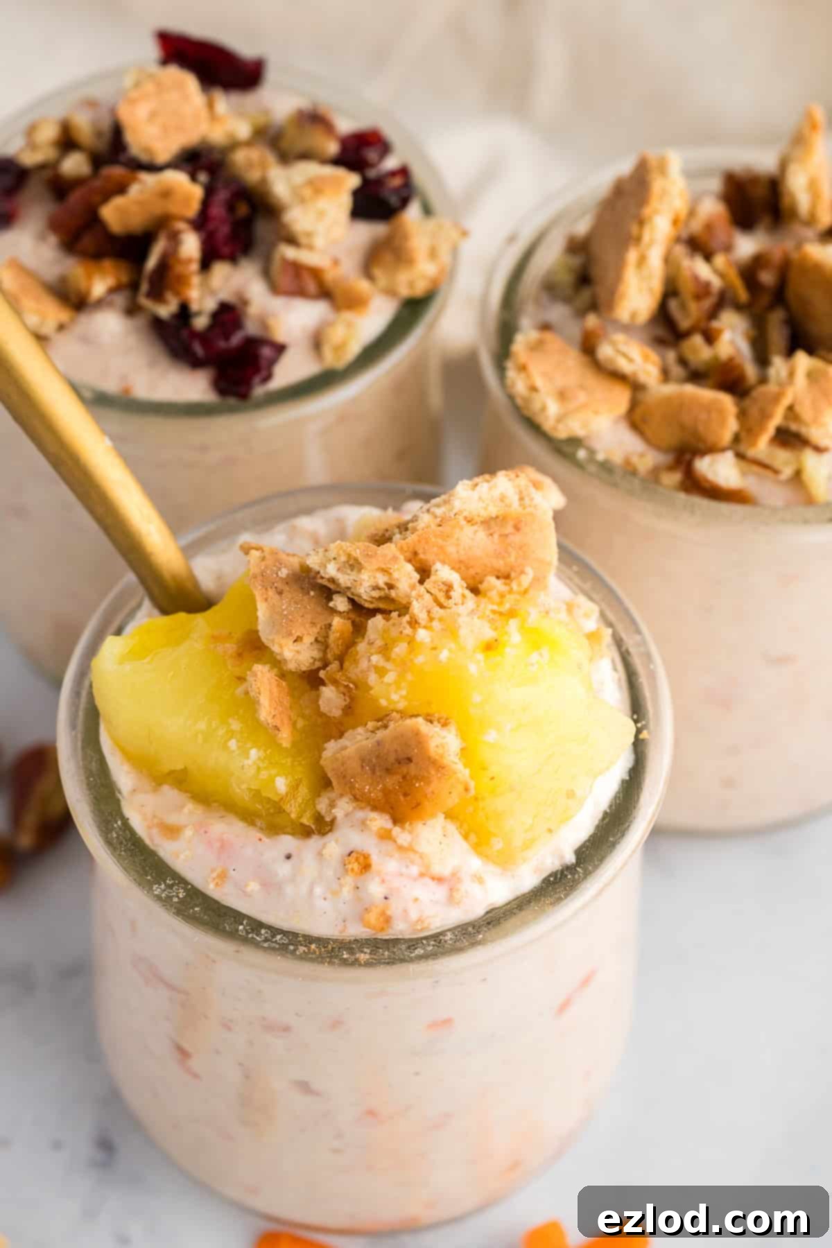 Carrot cake cheesecake cups in small jars topped with pineapple, graham crackers, and raisins.