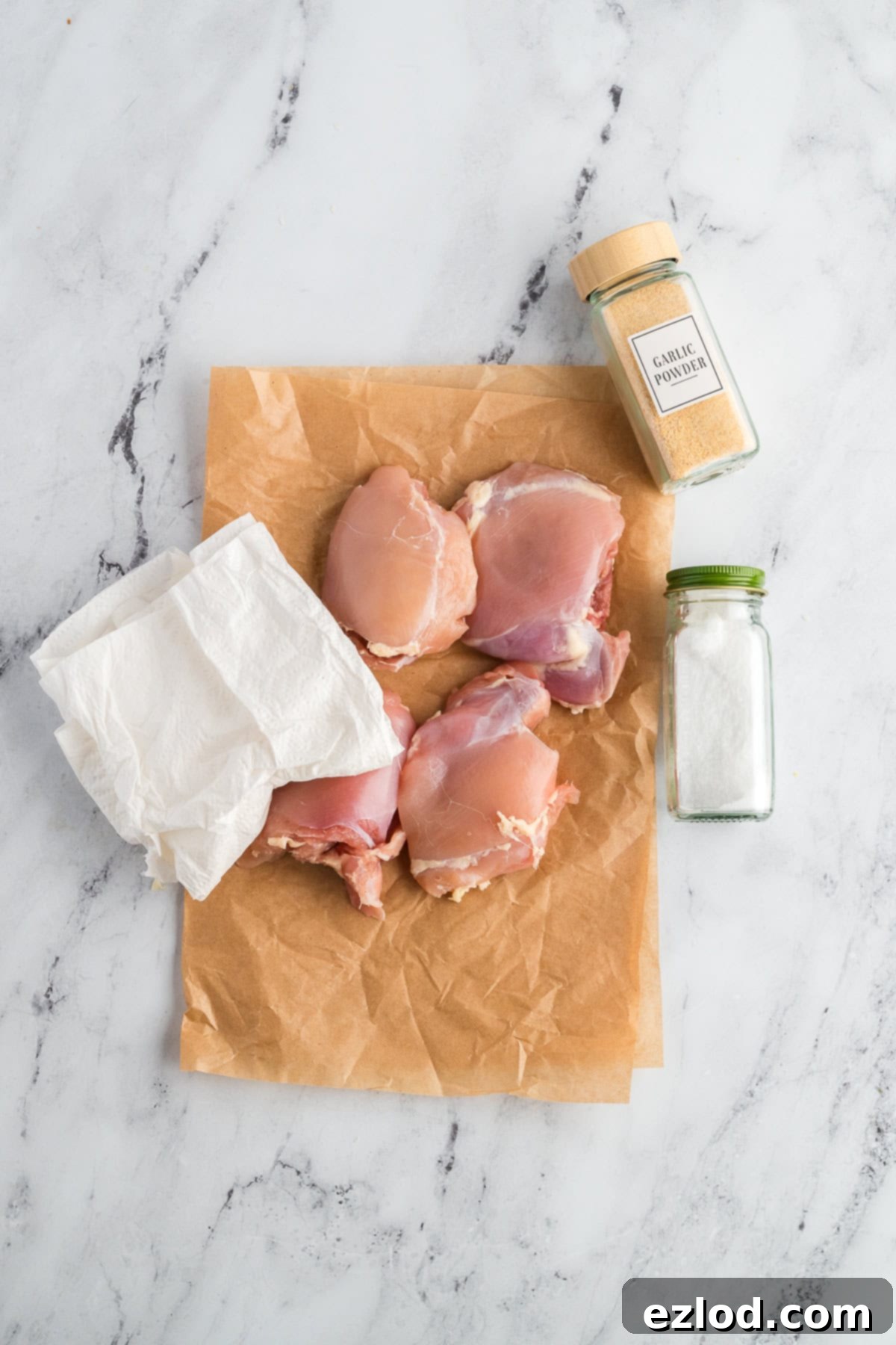 Your Go To One Pan Chicken Orzo 4 Chicken thighs on a piece of parchment before being seasoned with salt and garlic powder.
