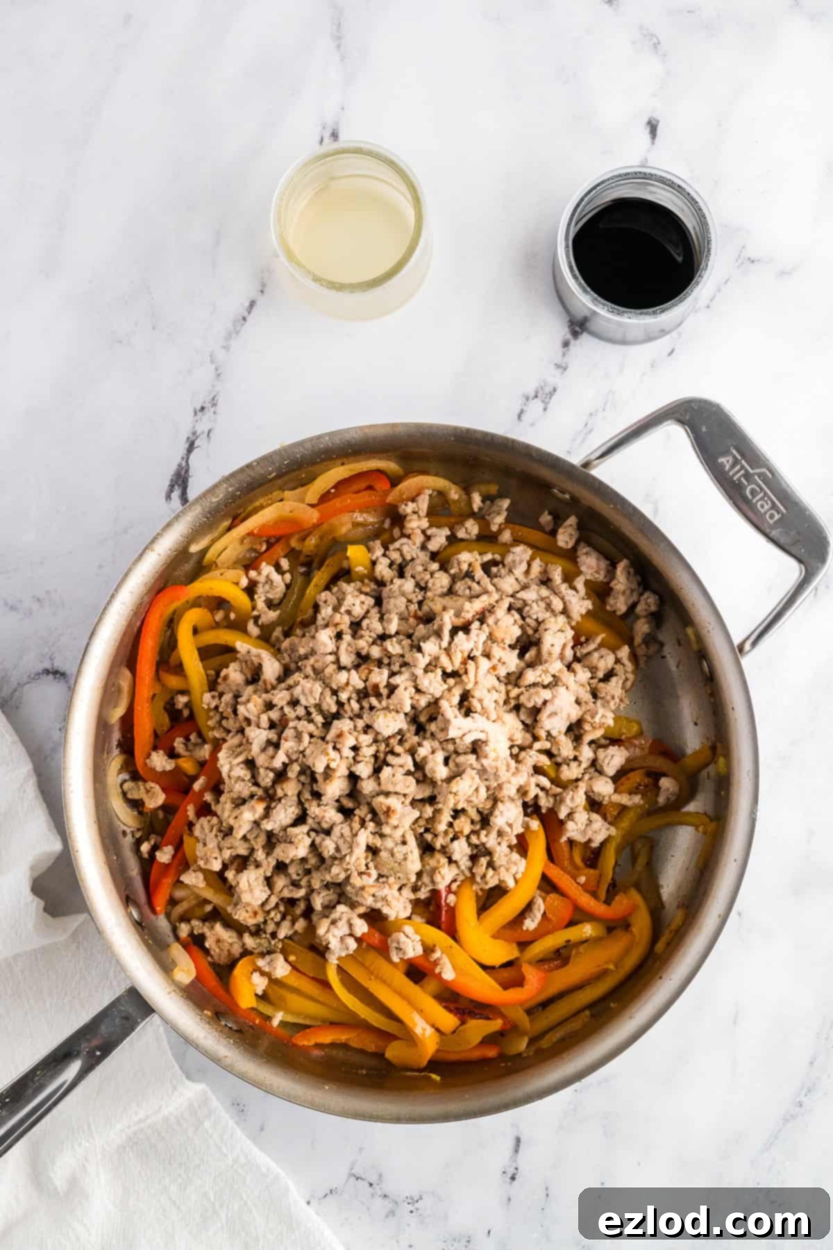 Cooked ground chicken, onions, and peppers combined in a stainless steel pan, being mixed together.